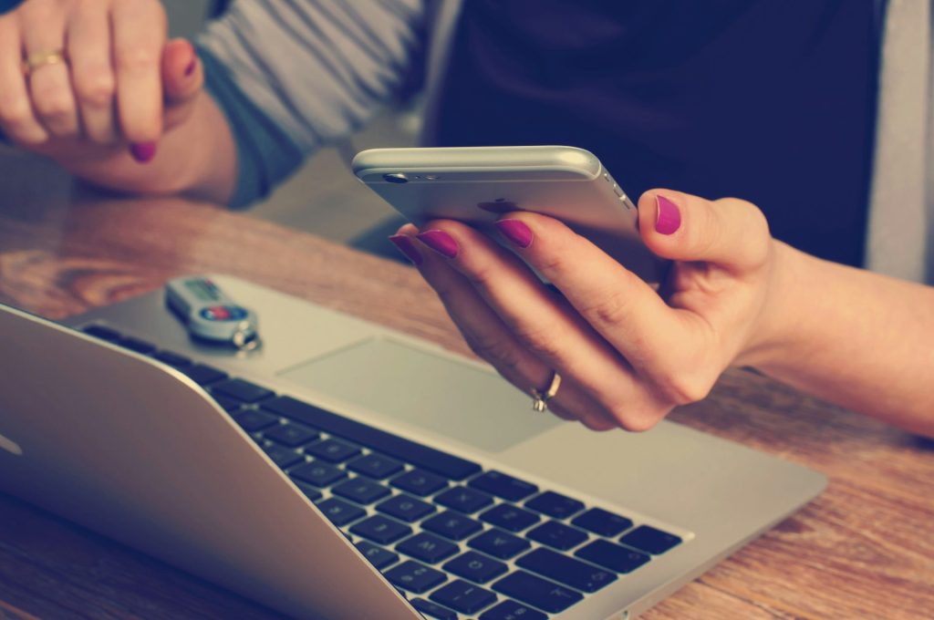 Person using a smartphone and laptop at a desk.